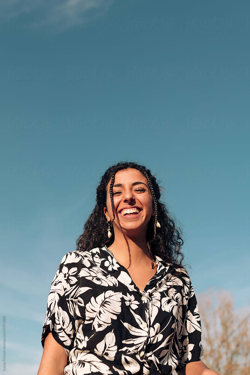 A woman laughing in warm daylight against a clear sky.
